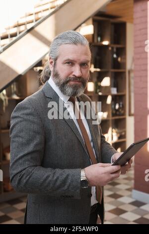 Portrait of confident mature businessman looking at camera while standing with tablet pc in the restaurant Stock Photo