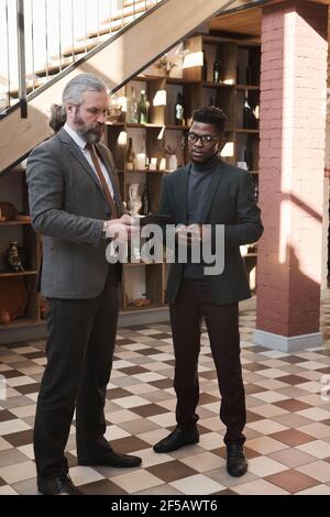 Two businessmen watching something on digital tablet while standing in the corridor of the restaurant Stock Photo