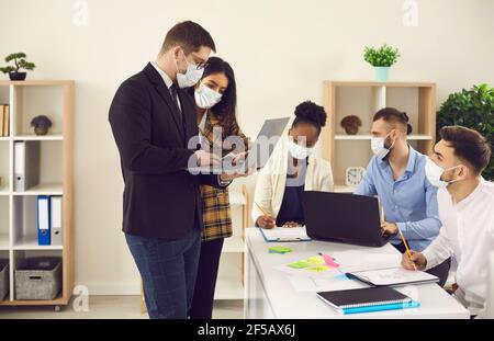 Young diverse company employees all wearing face masks working in office together Stock Photo