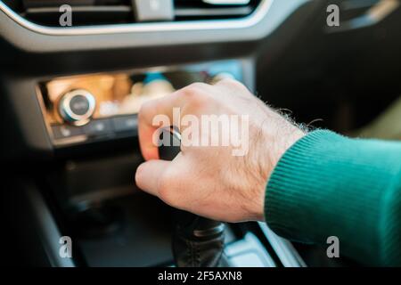 A mans hand shifting gearbox in the modern auto. Man shifting a stick of a manual or automatic gearbox.  Stock Photo