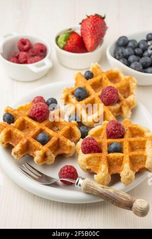 Top view of waffles with raspberries and blueberries, on plate with fork, and bowls with strawberries, raspberries and blueberries, selective focus, o Stock Photo