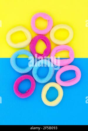 Multicolored little rubber bands for hair, on blue yellow paper background. Stock Photo