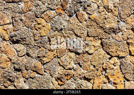 Texture of a rough masonry wall made of old weathered orange shell rock, illuminated by sunbeams with harsh shadows. Stock Photo