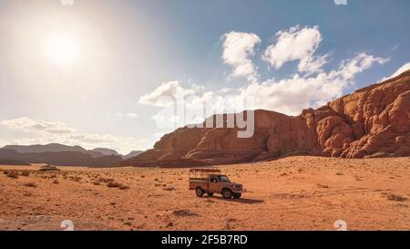 Dusty desert with rocky massif and blue sky above, off road desert vehicle in foreground. Typical scenery in Wadi Rum, Jordan Stock Photo