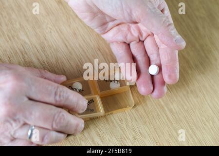 Closeup of an elderly senior woman's hands taking her medication for the week in a pill box on wooden table, business,health concept Stock Photo