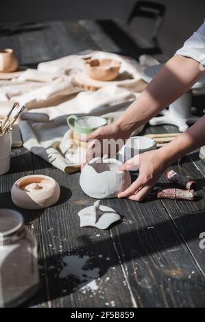 Female hands gently putting the finished glazed bowl on a wooden table with different pottery tools Stock Photo