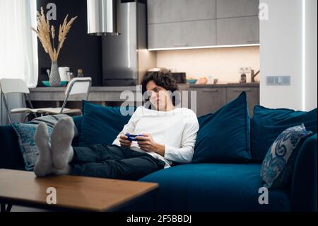 Bored young man playing video game while lying on sofa at home. Stock Photo