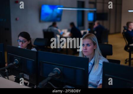 Group of Security data center operators (administrators) working in a group at a CCTV monitoring room while looking at multiple monitors ( computer sc Stock Photo