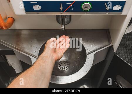 The guy brings his hand to the automatic water supply tap in the modern toilet of the stadler electric train. Stock Photo