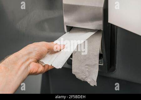 Man's hand takes or tears off toilet paper in a roll, close-up, soft focus. Stock Photo