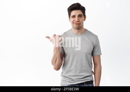 That is lame. Unimpressed and disappointed man pointing aside at bad offer, looking displeased and skeptical, standing over white background Stock Photo