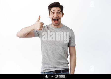 Nice job man, like it. Pleased good-looking happy male friend with brislte, showing thumbs up and smiling broadly, giving positive feedback, sharing Stock Photo