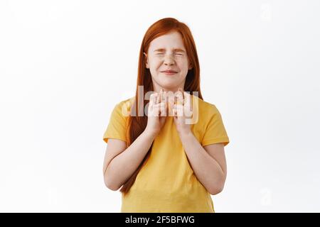 Cute redhead little girl, child making wish with fingers crossed, praying for something happen, dreaming, standing over white background Stock Photo