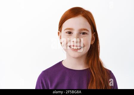 Close up portrait of beautiful red haired girl with freckles, smiling with teeth and looking happy at camera, positive emotion, joyful kid, white Stock Photo