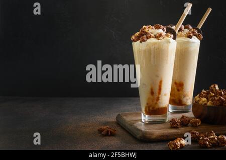 Tasty banana milkshake garnished with caramel, whipped cream, popcorn on dark background. Space for text. Stock Photo
