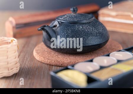 https://l450v.alamy.com/450v/2f5bkn8/black-metal-japanese-tea-pot-on-a-wooden-table-with-tea-candles-and-wooden-box-of-fragrant-sticks-zen-style-still-life-in-warm-peaceful-colors-hot-2f5bkn8.jpg