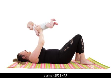 mother with baby having fun holding baby in the air while laying on a fitness mat Stock Photo