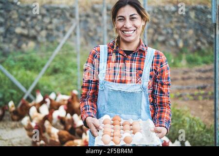Senior farmer woman picking up organic eggs in henhouse - Farm lifestyle and healthy food concept - Focus on face Stock Photo