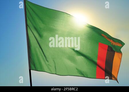 Zambia flag waving in the blue sky with green fields at mountain peak ...