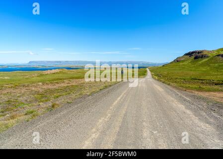 Straight unmade road running along the coast on a clear summer day. Beautiful blue sky. Stock Photo