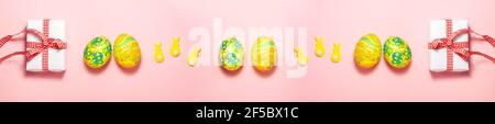Banner of Easter green and yellow eggs, white gift box with red gift bow and yellow velvet rabbits with white tails on bright pink background. Flat la Stock Photo