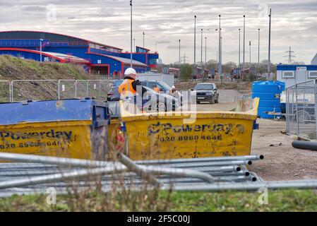 builder stands next to industrial skip taking a break , Dockland light railway track, Greater London Stock Photo
