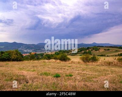 Massive dark heavy rain clouds over a hilly landscape with a town in the valley Stock Photo