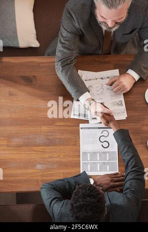 High angle view of two businessmen sitting at the table discussing business contract and shaking hands to conclude a deal Stock Photo