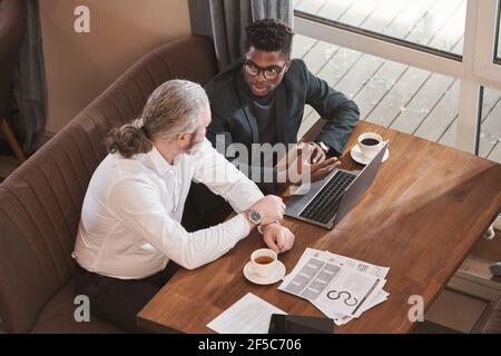 High angle view of businessmen sitting at the table using laptop and discussing contract during a meeting in the restaurant Stock Photo