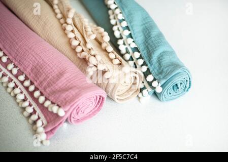 Three rolls of muslin cotton towels in pastel colors. Decorated with braid with pompons. Stock Photo