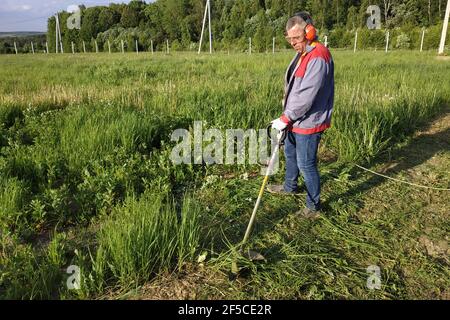 Man mows the grass with a trimmer, tall grass in a meadow, handmade in the garden.new Stock Photo