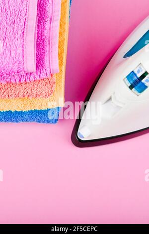 The concept of ironing clothes. House order. Iron and ironed fabric. Electric iron on a pink background with towels. multi-colored towels Stock Photo