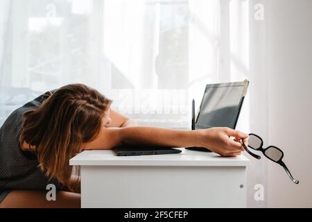 Young woman sleeping in the workplace. Fatigue and overload in office work. Side view. Stock Photo