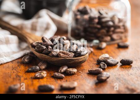 Roasted cocoa beans in wooden spoon on wooden table. Stock Photo