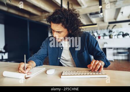 Handsome curly guy is making notes at the working table in open space office Stock Photo