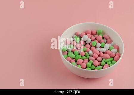 Sweet Dragee in a white bowl on a pink background. Peanuts covered with sugar glaze. White, pink, green. Selective focus. Copy space Stock Photo