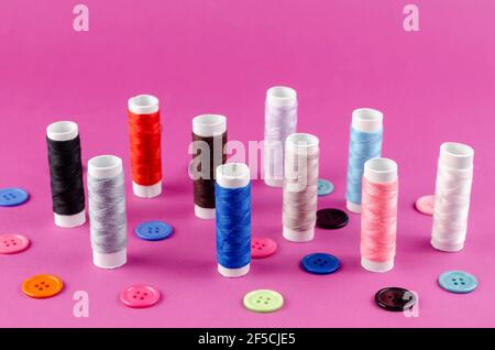 Multicolored thread spools and buttons on purple background. A set of thread stands vertically. Ten spools. Random buttons. View from above at an angl Stock Photo