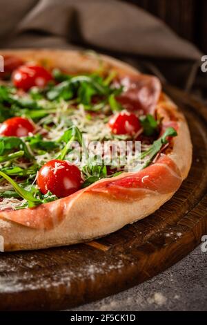 Pizza close up with arugula, prosciutto and cherry tomatoes on a wooden board. Photo for the menu. Stock Photo