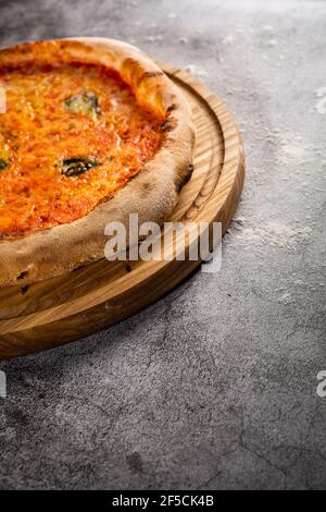 Wooden board with pizza on a concrete background. Advertising shooting. Photo for the menu. Stock Photo