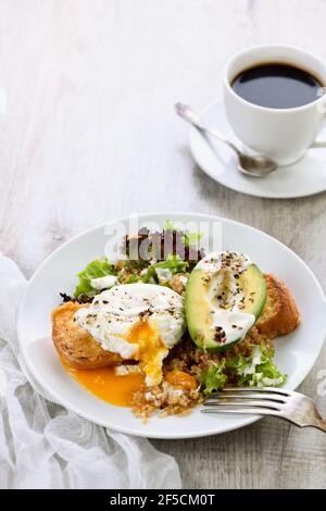 A healthy and balanced breakfast plate. Benedict's egg spreads on a toasted toast with half an avocado, quinoa and lettuce, seasoned   spices and yogu Stock Photo