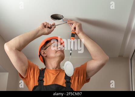 The electrician is installing an LED spotlight in the ceiling. Stock Photo