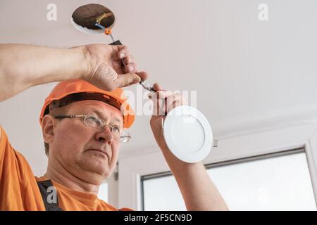 The electrician is installing an LED spotlight in the ceiling. Stock Photo