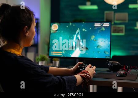 Caucasian woman holding wireless joystick and playing virtual videogames. Virtual streaming cyber performing live tournament using professional equipment in gaming home studio Stock Photo