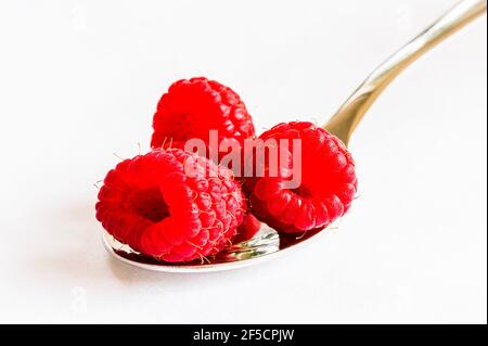Close-up of red raspberries on a silver spoon on a white tablecloth, London, UK Stock Photo