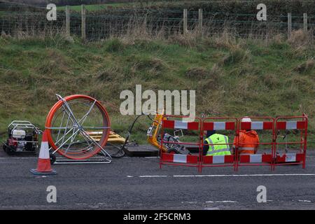A reel of fiber-optic cable is fed into a manhole during the installation of rural fiber-optic cables outside Lisburn, Northern Ireland, UK Stock Photo