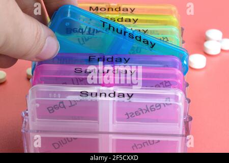 Pill box reminder, hand taking medicine daily pills in colorful box on pink background, elderly,senior,business,health,medication concept modern Stock Photo