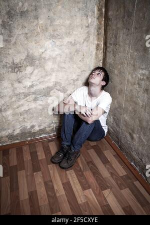 Toned Photo of Young Man in the Corner on the Floor by the Old Wall Stock Photo