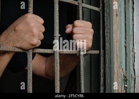 Human hands on rusty cage bars, close up shot Stock Photo