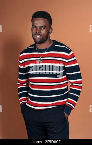 Stock photo of young black man posing in studio shot and looking at camera over brown background. Stock Photo