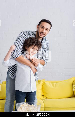 happy muslim man hugging excited son showing win gesture and looking at camera Stock Photo